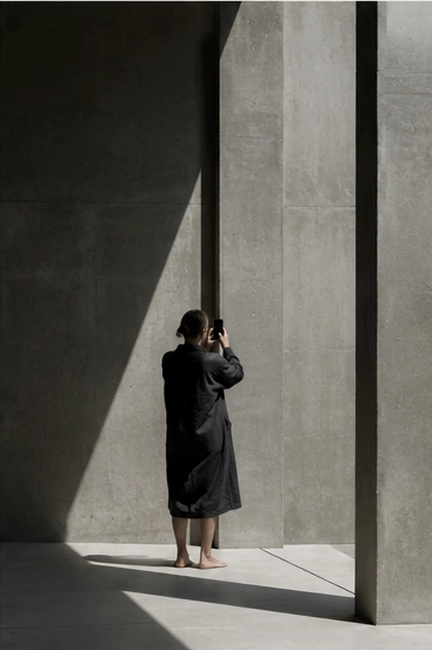 A woman photographing light and shadow in monumental concrete architecture